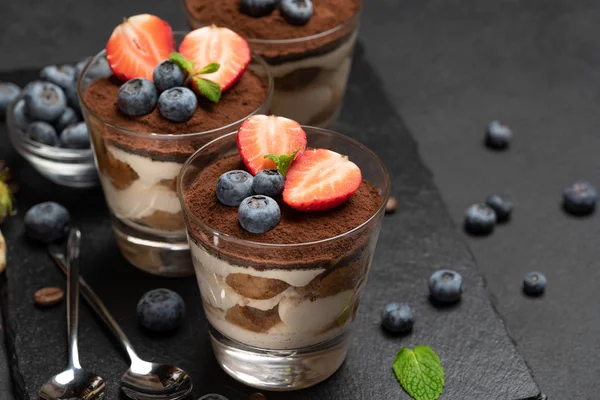 Dessert tiramisù classico con mirtilli e fragole in un bicchiere su sfondo di cemento scuro — Foto Stock