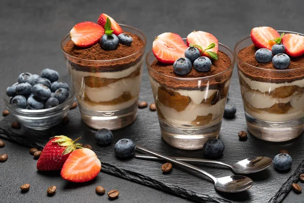 Klassisches Tiramisu-Dessert mit Blaubeeren und Erdbeeren im Glas auf dunklem Betongrund — Stockfoto