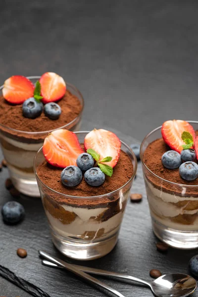 Klassiek Tiramisu-dessert met bosbessen en aardbeien in een glas op een donkere betonnen achtergrond — Stockfoto