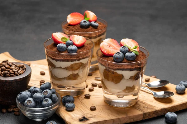 Klasyczny deser Tiramisu z jagodami i truskawkami w szklance na ciemnym betonowym tle — Zdjęcie stockowe