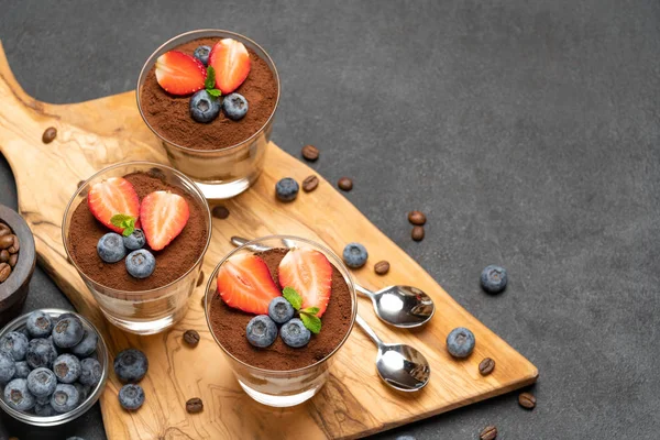 Sobremesa tiramisu clássica com mirtilos e morangos em um copo no fundo de concreto escuro — Fotografia de Stock