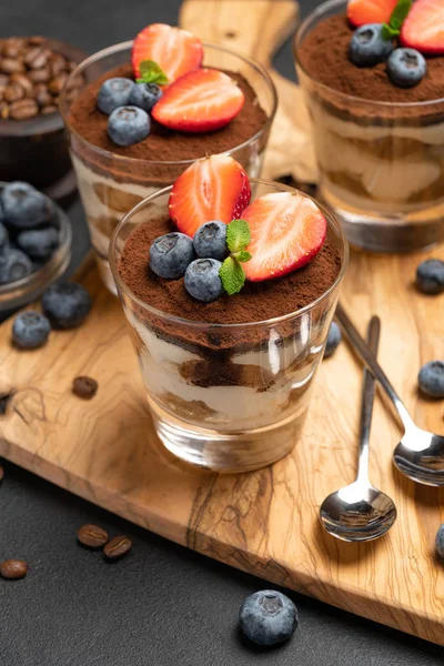 Класичний десерт тірамісу з чорницею та полуницею у склянці на темному бетонному фоні — стокове фото