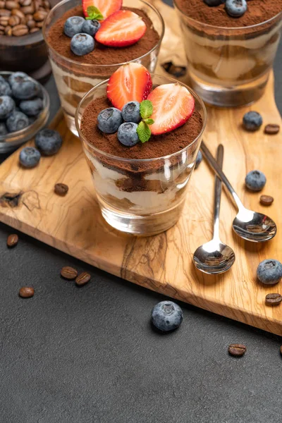 Klassiek Tiramisu-dessert met bosbessen en aardbeien in een glas op een donkere betonnen achtergrond — Stockfoto