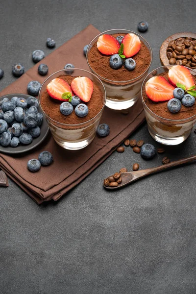 Classic tiramisu dessert with blueberries and strawberries in a glass on dark concrete background — Stock Photo, Image