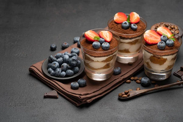Dessert tiramisù classico con mirtilli e fragole in un bicchiere su sfondo di cemento scuro — Foto Stock