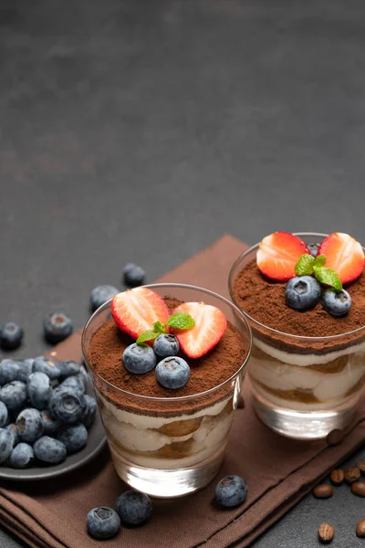 Класичний десерт тірамісу з чорницею та полуницею у склянці на темному бетонному фоні — стокове фото