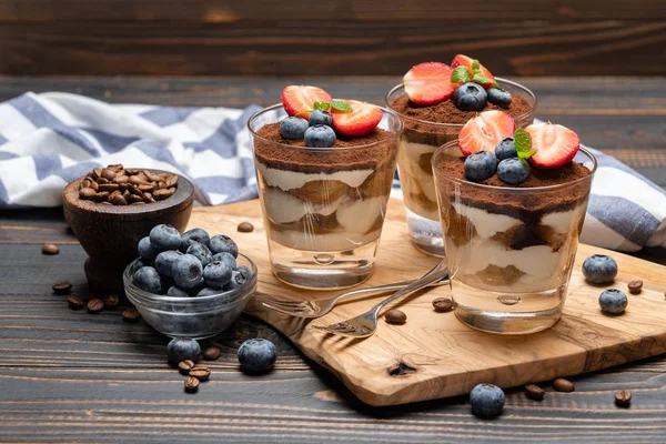 Sobremesa tiramisu clássica com mirtilos e morangos em um copo no fundo de madeira — Fotografia de Stock