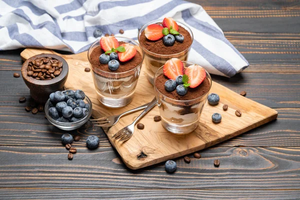 Classic tiramisu dessert with blueberries and strawberries in a glass on wooden background — Stock Photo, Image