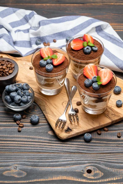 Sobremesa tiramisu clássica com mirtilos e morangos em um copo no fundo de madeira — Fotografia de Stock