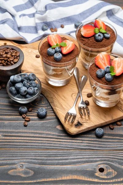 Sobremesa tiramisu clássica com mirtilos e morangos em um copo no fundo de madeira — Fotografia de Stock