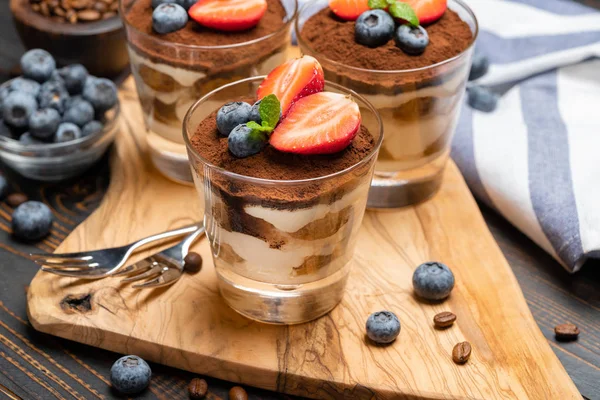 Classic tiramisu dessert with blueberries and strawberries in a glass on wooden background — Stock Photo, Image