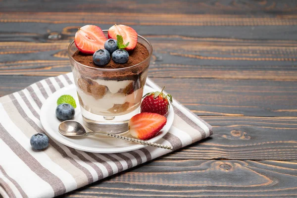 Klassisk tiramisu dessert med blåbär och jordgubbar i ett glas på trä bakgrund — Stockfoto