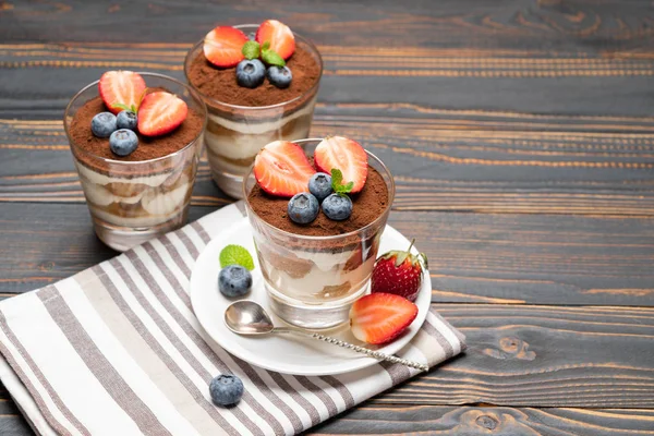 Классический десерт тирамису с черникой и клубникой в стакане на деревянном фоне — стоковое фото