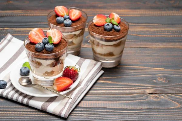 Klassisches Tiramisu-Dessert mit Blaubeeren und Erdbeeren im Glas auf Holzgrund — Stockfoto