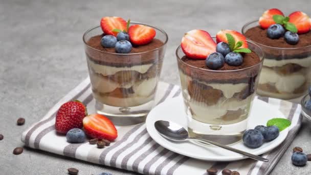 Klassisches Tiramisu-Dessert mit Blaubeeren und Erdbeeren im Glas auf Betongrund — Stockvideo