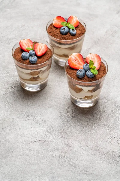 Sobremesa tiramisu clássica com mirtilos e morangos em um copo no fundo de concreto — Fotografia de Stock