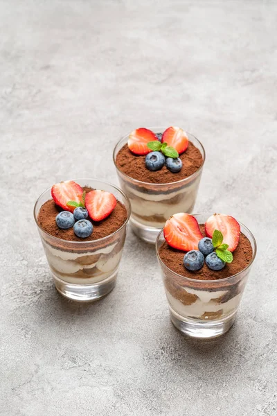 Classic tiramisu dessert with blueberries and strawberries in a glass on concrete background — Stock Photo, Image