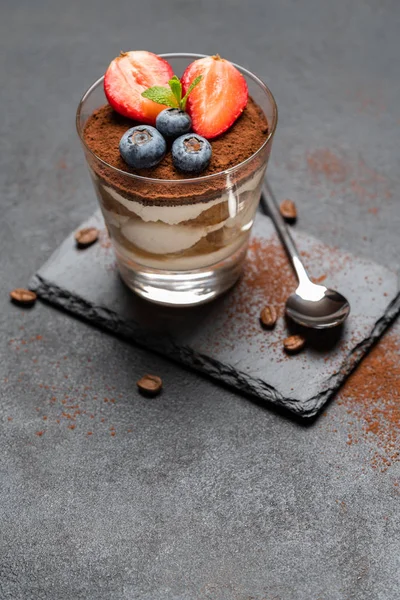 Klasszikus tiramisu desszert áfonyával és eper egy pohár kő szolgáló hajón sötét beton háttér — Stock Fotó