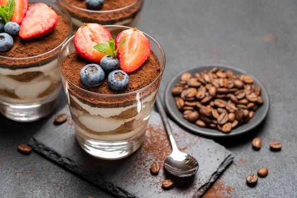 Klassiek Tiramisu-dessert met bosbessen en aardbeien in een glas op steen serveren bord op donkere betonnen achtergrond — Stockfoto