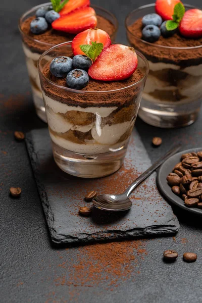 Класичний десерт тірамісу з чорницею та полуницею у склянці на кам'яній дошці на темному бетонному фоні — стокове фото