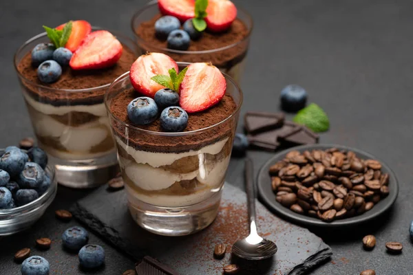 Sobremesa tiramisu clássica com mirtilos e morangos em um copo em placa de pedra no fundo de concreto escuro — Fotografia de Stock