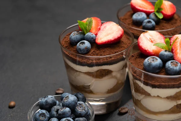 Klassisches Tiramisu-Dessert mit Blaubeeren und Erdbeeren im Glas auf Steinplatte auf dunklem Betongrund — Stockfoto