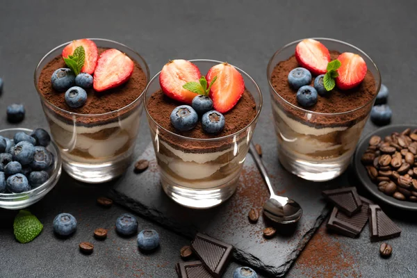 Classic tiramisu dessert with blueberries and strawberries in a glass on stone serving board on dark concrete background — Stock Photo, Image