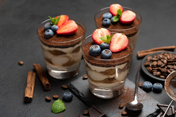 Klassisches Tiramisu-Dessert mit Blaubeeren und Erdbeeren im Glas auf Steinplatte auf dunklem Betongrund — Stockfoto