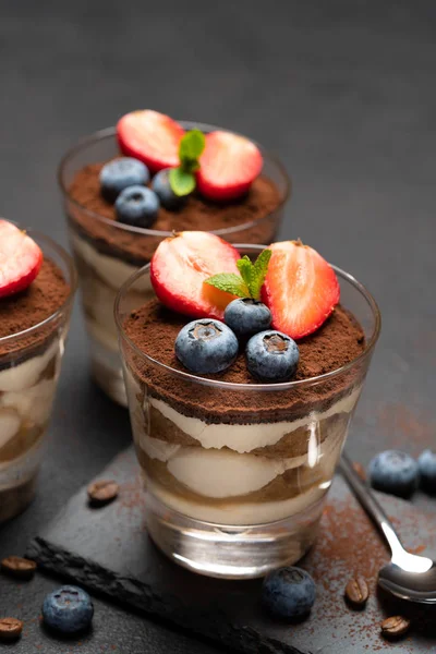 Klassiek Tiramisu-dessert met bosbessen en aardbeien in een glas op steen serveren bord op donkere betonnen achtergrond — Stockfoto