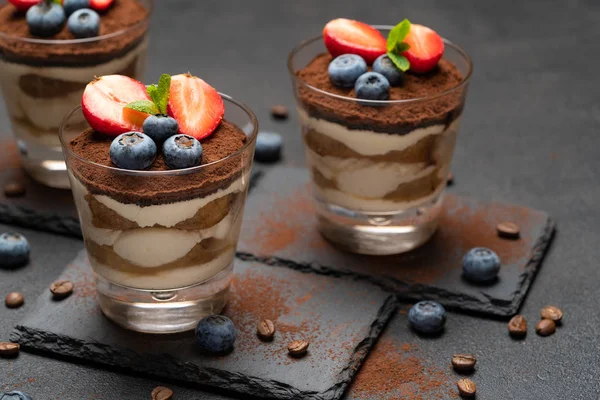 Klassisches Tiramisu-Dessert mit Blaubeeren und Erdbeeren im Glas auf Steinplatte auf dunklem Betongrund — Stockfoto