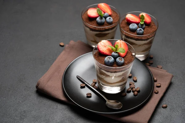 Classic tiramisu dessert with blueberries and strawberries in a glass on stone serving board on dark concrete background — Stock Photo, Image