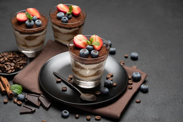 Sobremesa tiramisu clássica com mirtilos e morangos em um copo em placa de pedra no fundo de concreto escuro — Fotografia de Stock