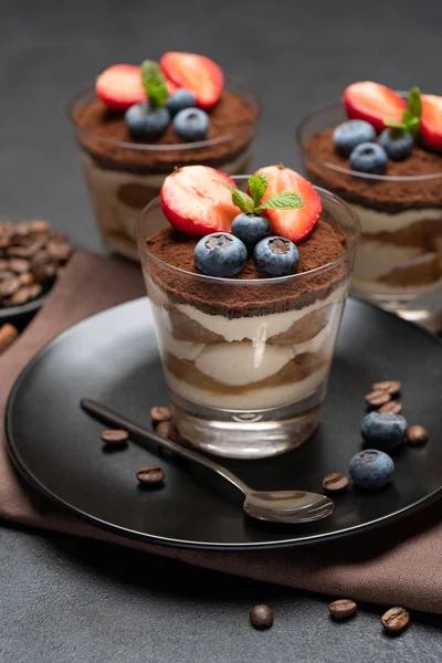 Klassisches Tiramisu-Dessert mit Blaubeeren und Erdbeeren im Glas auf Steinplatte auf dunklem Betongrund — Stockfoto