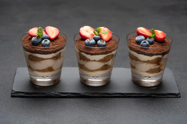 Klassisches Tiramisu-Dessert mit Blaubeeren und Erdbeeren im Glas auf Steinplatte auf dunklem Betongrund — Stockfoto