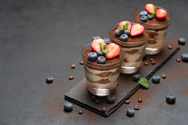 Klassisches Tiramisu-Dessert mit Blaubeeren und Erdbeeren im Glas auf Steinplatte auf dunklem Betongrund — Stockfoto