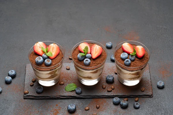 Klassisches Tiramisu-Dessert mit Blaubeeren und Erdbeeren im Glas auf Steinplatte auf dunklem Betongrund — Stockfoto