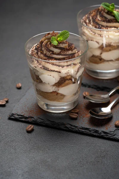 Sobremesa tiramisu clássico em um copo em pedra servindo placa no fundo de concreto escuro — Fotografia de Stock