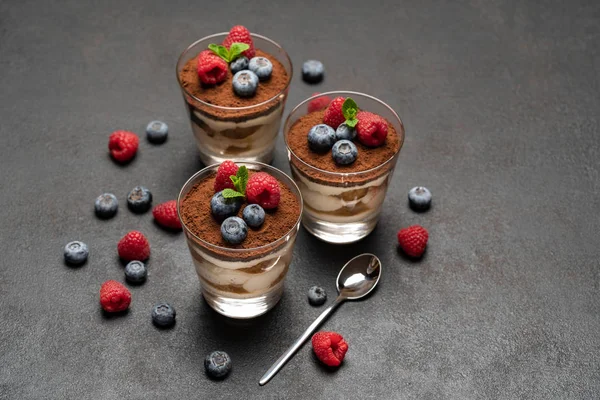 Класичний десерт тірамісу з чорницею та малиною у склянці на темному бетонному фоні — стокове фото
