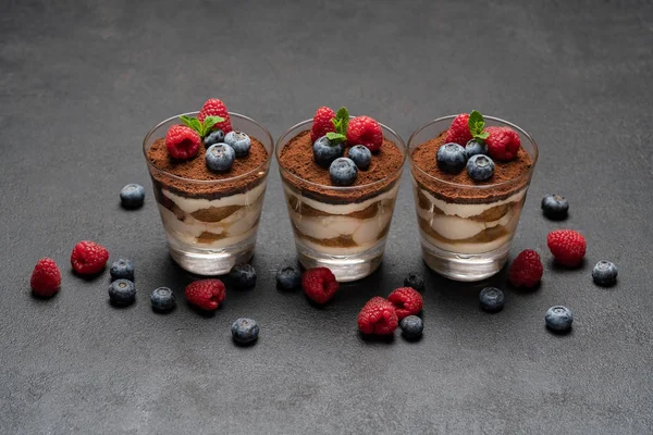 Класичний десерт тірамісу з чорницею та малиною у склянці на темному бетонному фоні — стокове фото