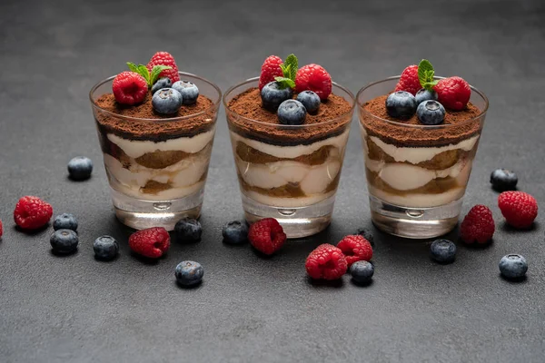 Klassisches Tiramisu-Dessert mit Blaubeeren und Himbeeren im Glas auf dunklem Betongrund — Stockfoto