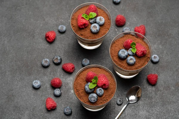 Klassisches Tiramisu-Dessert mit Blaubeeren und Himbeeren im Glas auf dunklem Betongrund — Stockfoto