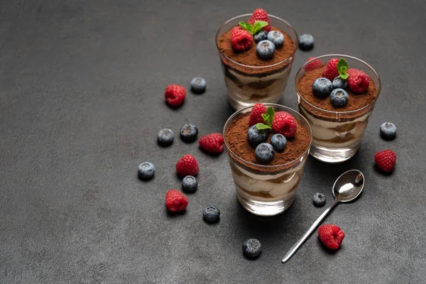 Klassisches Tiramisu-Dessert mit Blaubeeren und Himbeeren im Glas auf dunklem Betongrund — Stockfoto