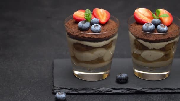 Классический десерт из тирамису с черникой и клубникой в стакане на каменной доске — стоковое видео