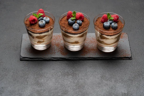 Klassisches Tiramisu-Dessert mit Blaubeeren und Himbeeren im Glas auf Steinplatte auf dunklem Betongrund — Stockfoto