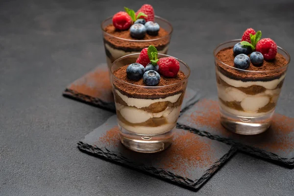 Classic tiramisu dessert with blueberries and raspberries in a glass on stone serving board on dark concrete background — Stock Photo, Image