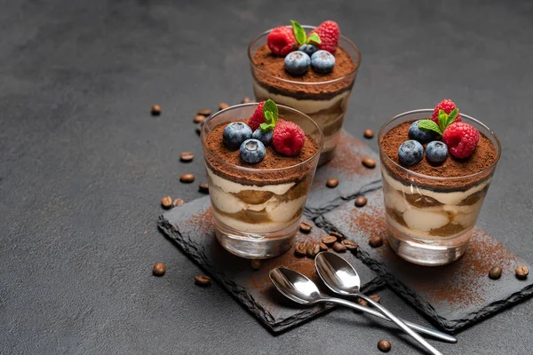 Sobremesa tiramisu clássico com mirtilos e framboesas em um copo em pedra servindo placa no fundo de concreto escuro — Fotografia de Stock