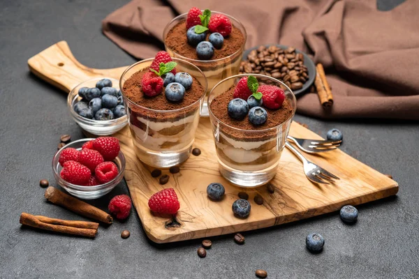 Klassiek Tiramisu-dessert met bosbessen en frambozen in een glas op steen serveerplank op een donkere betonnen achtergrond — Stockfoto