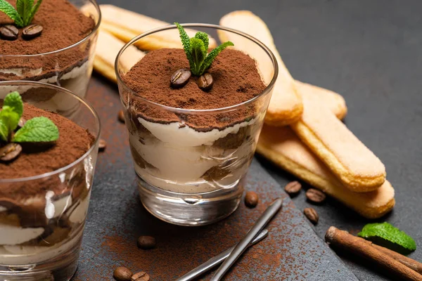 Postre tiramisú clásico en un vaso y galletas savoiardi sobre tabla de servir de piedra sobre fondo de hormigón oscuro —  Fotos de Stock