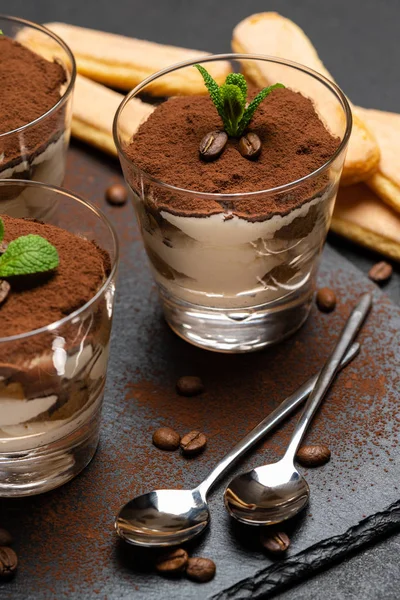 Classico dessert tiramisù in bicchiere e biscotti savoiardi su tavola da portata in pietra su fondo di cemento scuro — Foto Stock