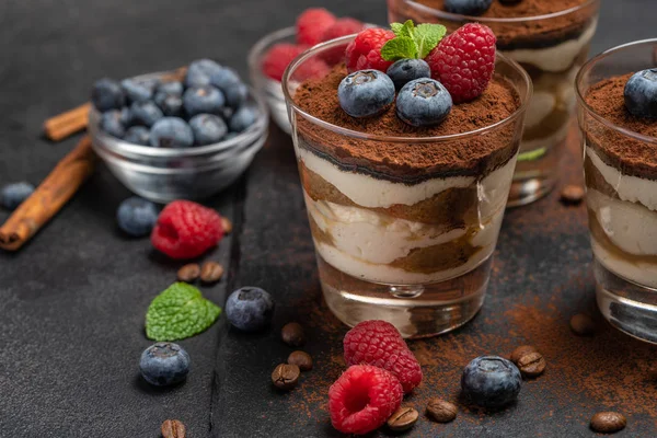 Klassisches Tiramisu-Dessert mit Blaubeeren und Himbeeren im Glas auf Steinplatte auf dunklem Betongrund — Stockfoto